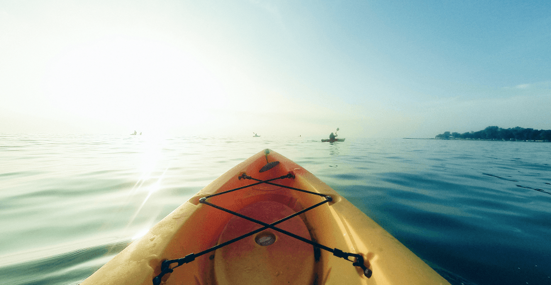 カヤックの先端越しに穏やかな水面と朝日の光が広がるイメージ