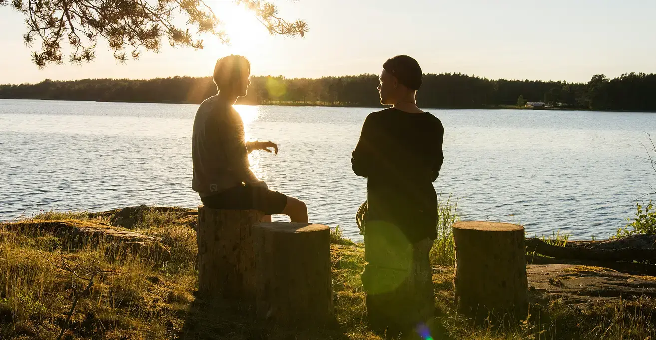 夕暮れ時の美しい水辺で、切り株に座って語り合う二人の男性