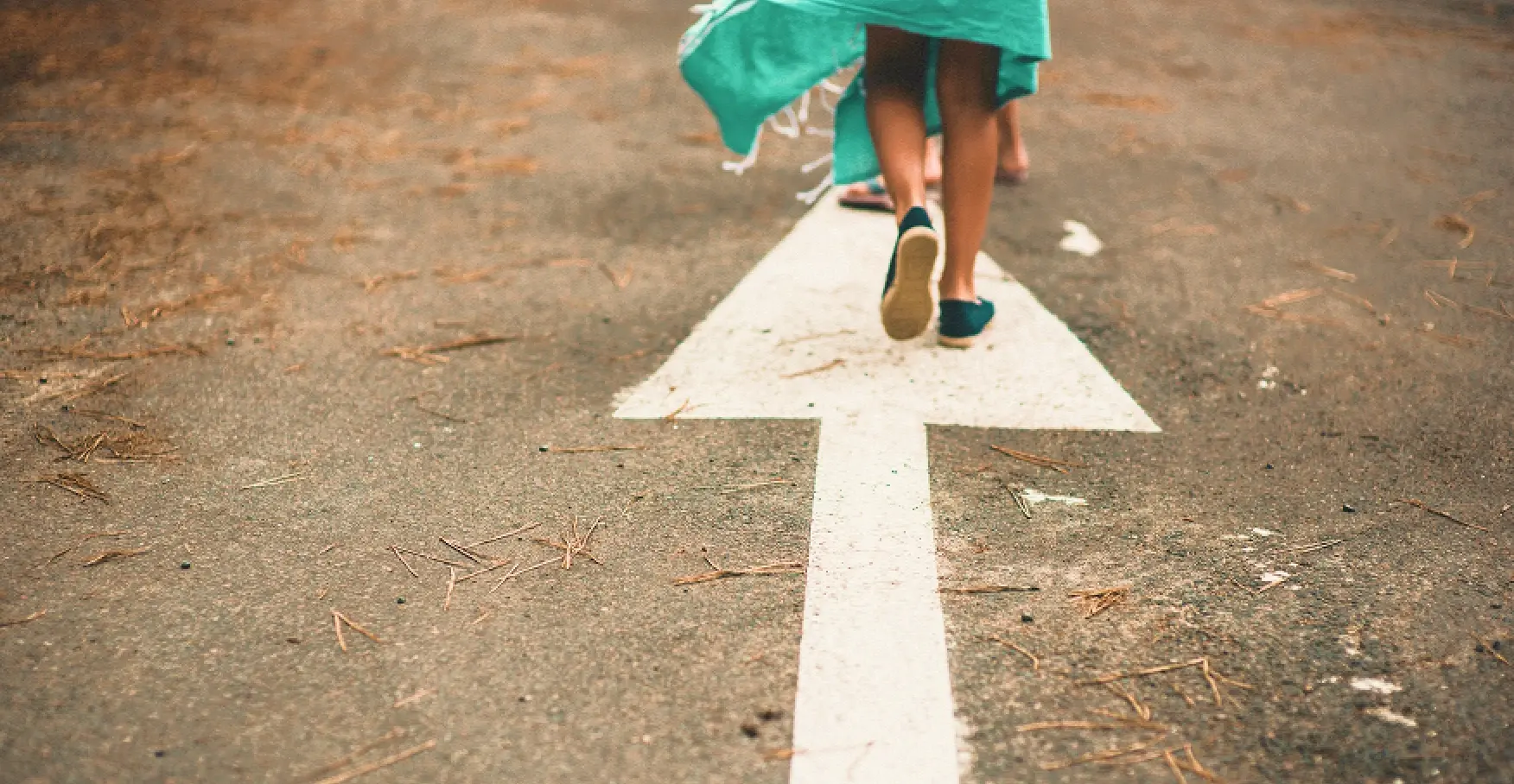 地面に描かれた白い矢印の上を、スカートの裾を揺らしながら前へ歩いていく人物の足元のイメージ