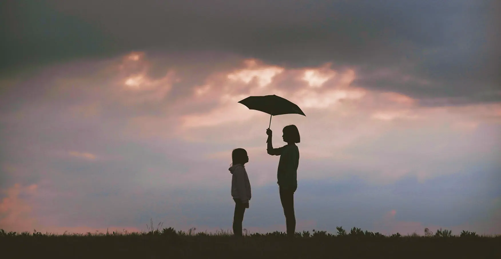 夕暮れの空の下で傘を差し出すシルエットのイメージ