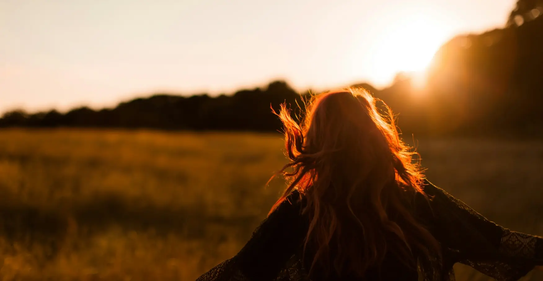 夕陽に照らされながら草原を歩く女性の後ろ姿