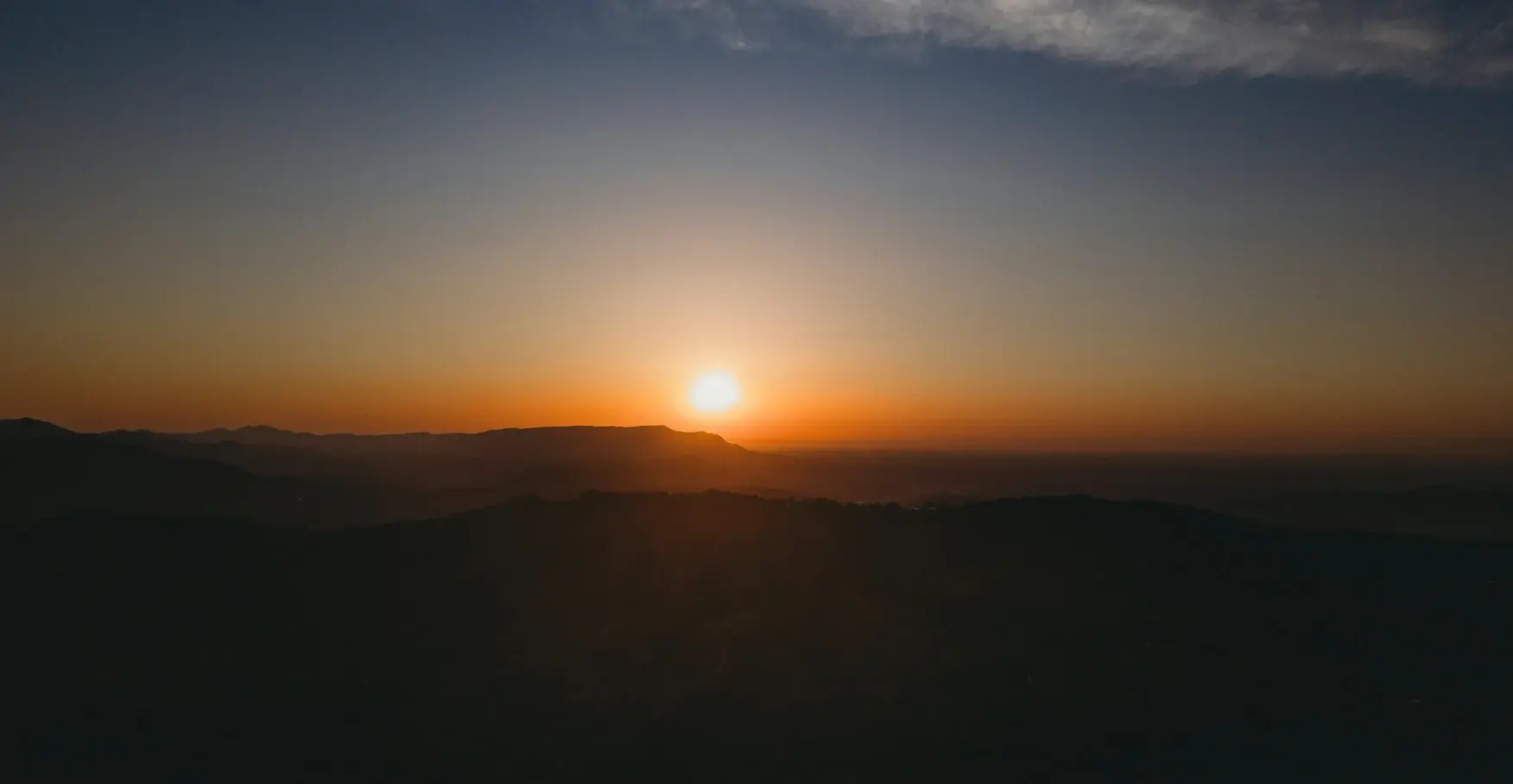 山並みの向こう側に沈むオレンジ色の明るい夕日