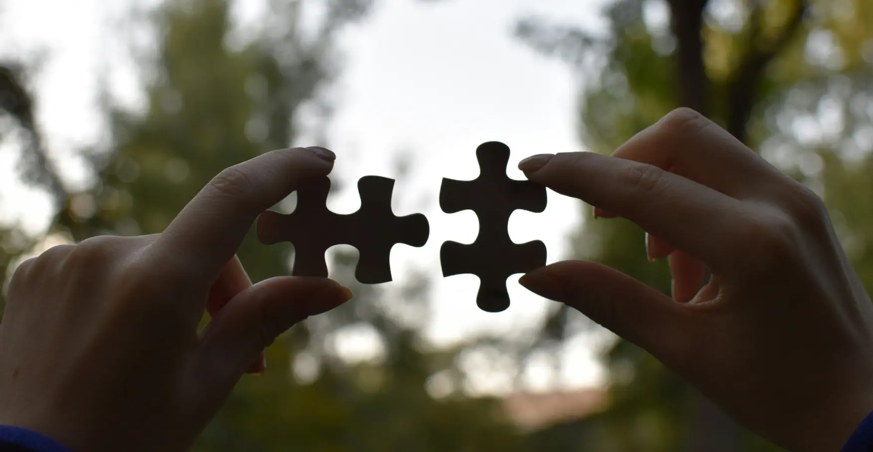 空を背景に二つのパズルピースを合わせようとする両手