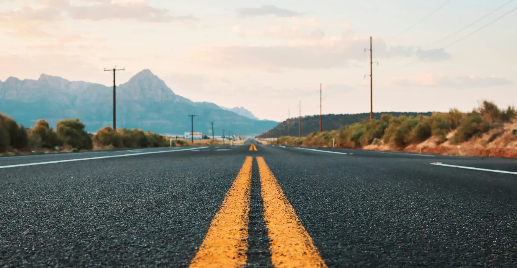 山並みに向かって真っ直ぐ伸びる、黄色い中央線があるアスファルトの道路