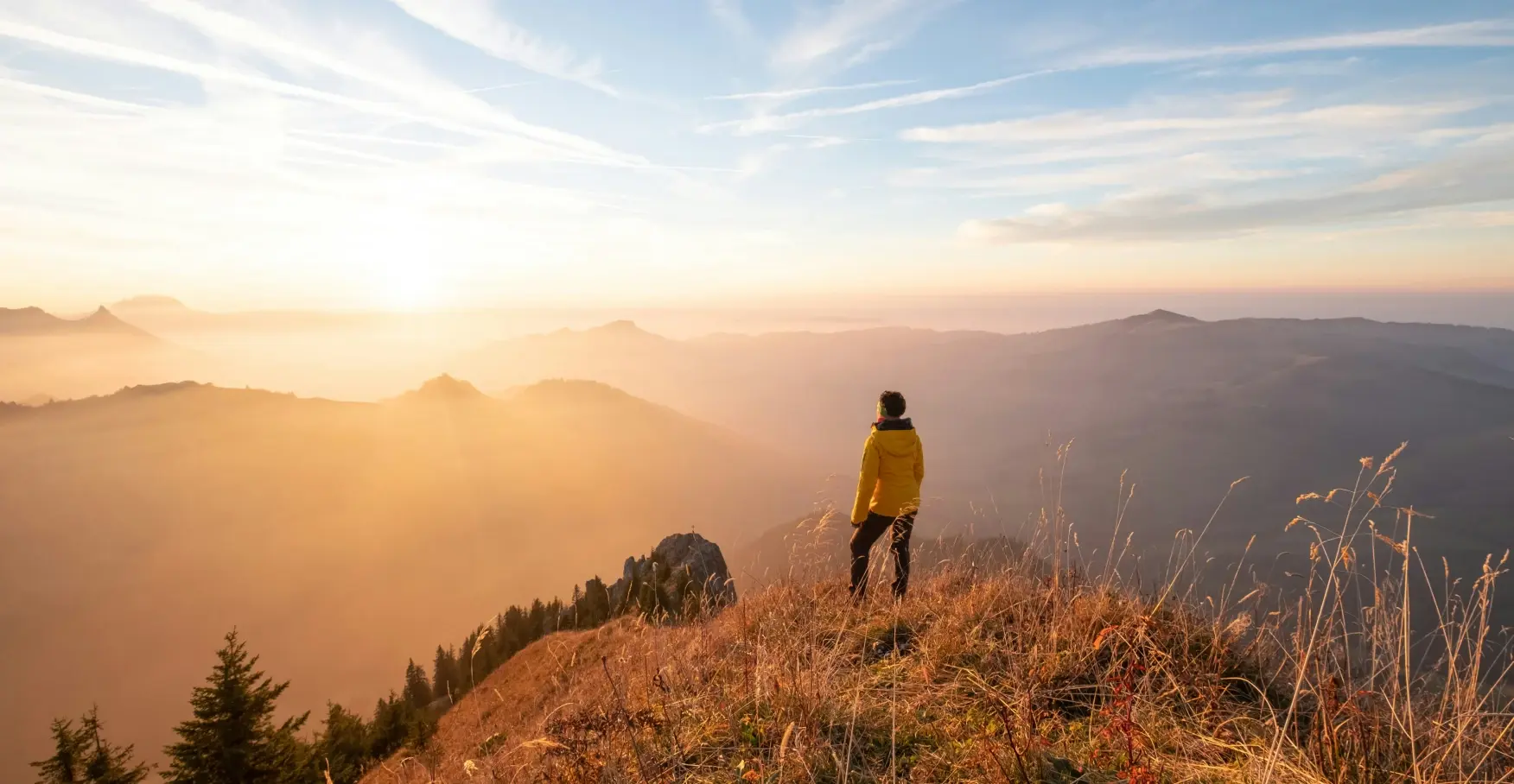 黄金色の朝日に包まれた山頂に立ち、雲海を見下ろす登山者の後ろ姿