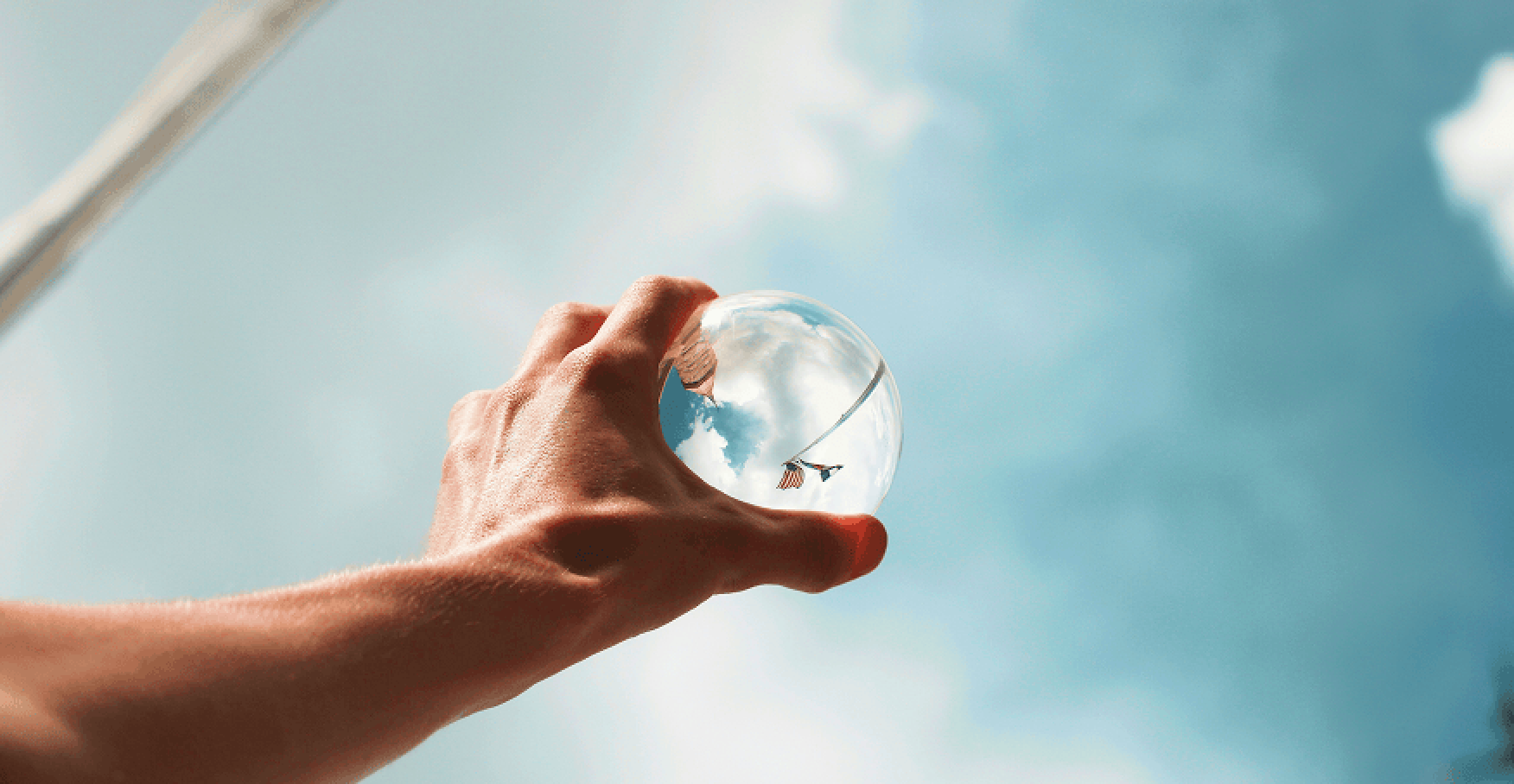 手に持った透明な球に空が映り込むイメージ