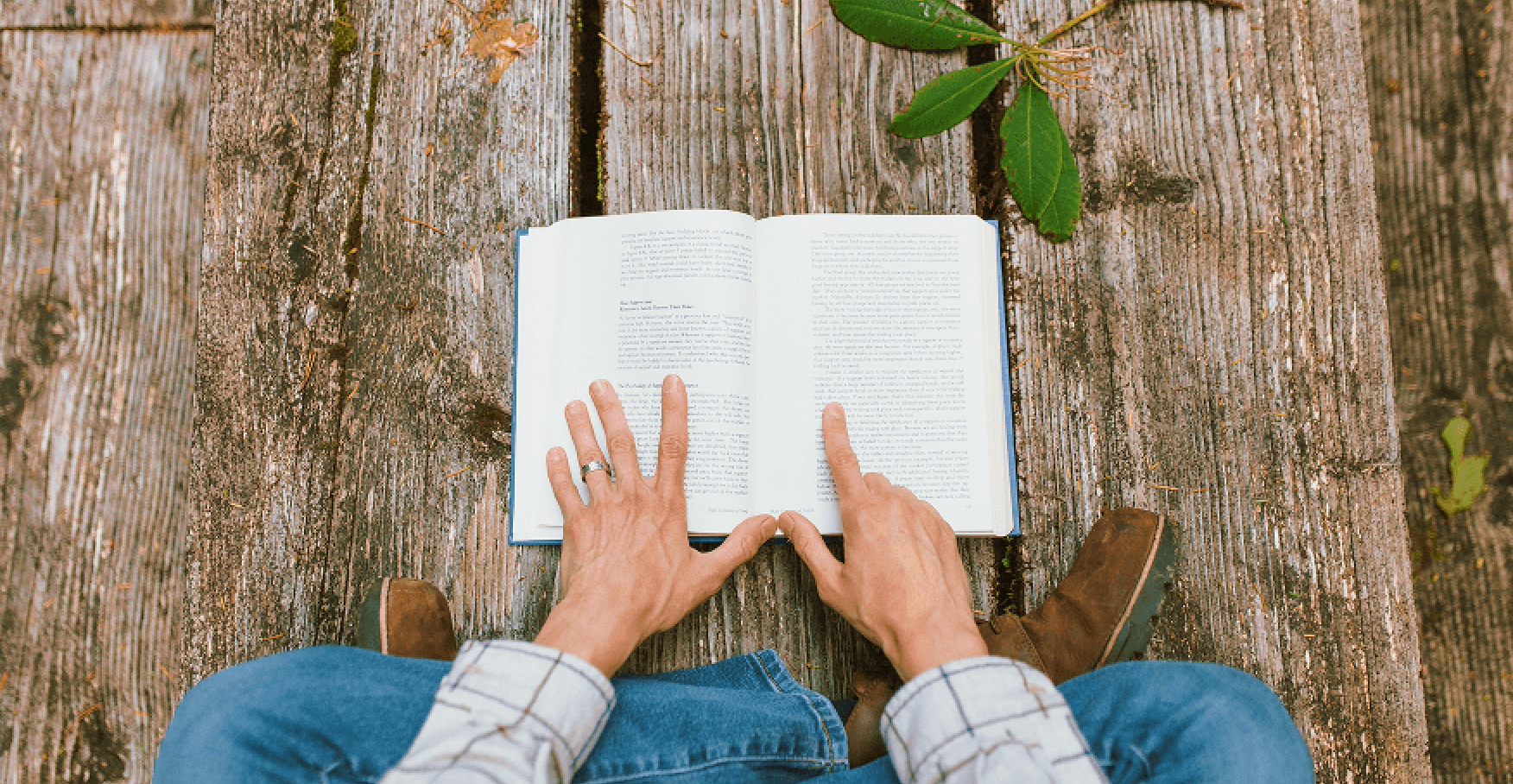 木のデッキに座って本を読み進める手元のイメージ