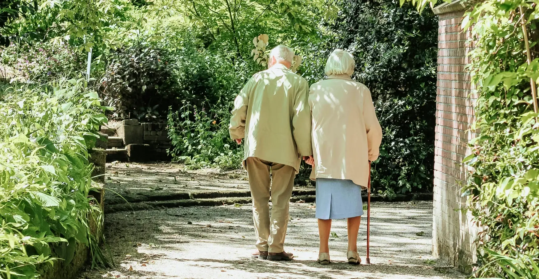 木漏れ日の小道を寄り添って歩く老夫婦のイメージ