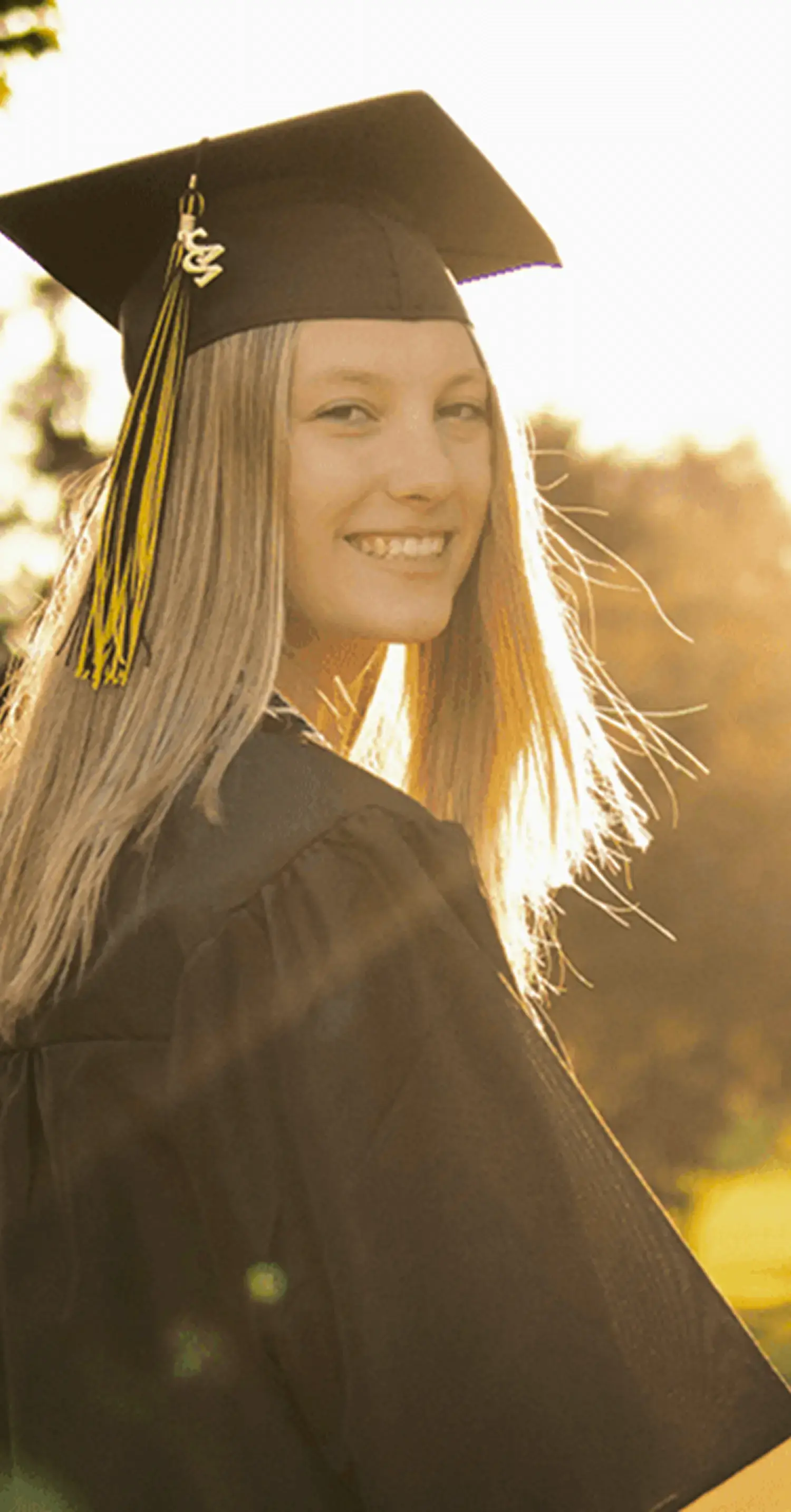 卒業式のアカデミックドレス(ガウンと角帽)を着用し、夕暮れの公園で微笑む女性_メインビジュアル_sp