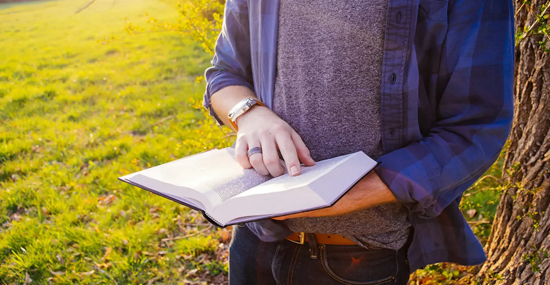 陽光が差し込む野原で本を読む、青いチェック柄のシャツを着た男性