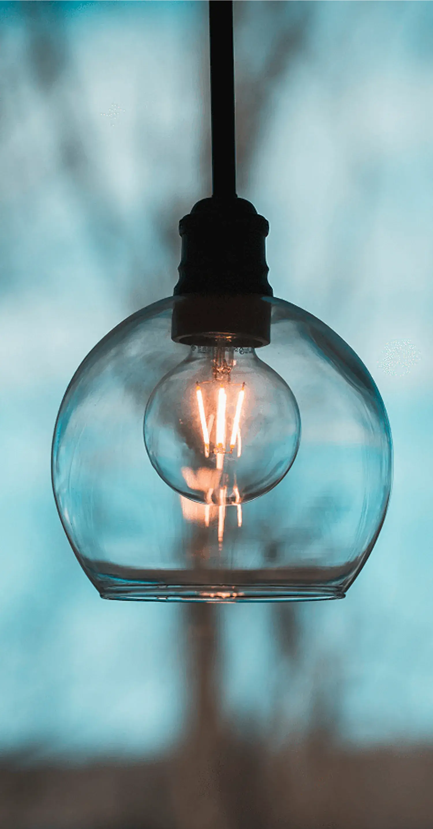青い背景をバックに吊るされた、フィラメントが光るガラス電球_メインビジュアル_sp