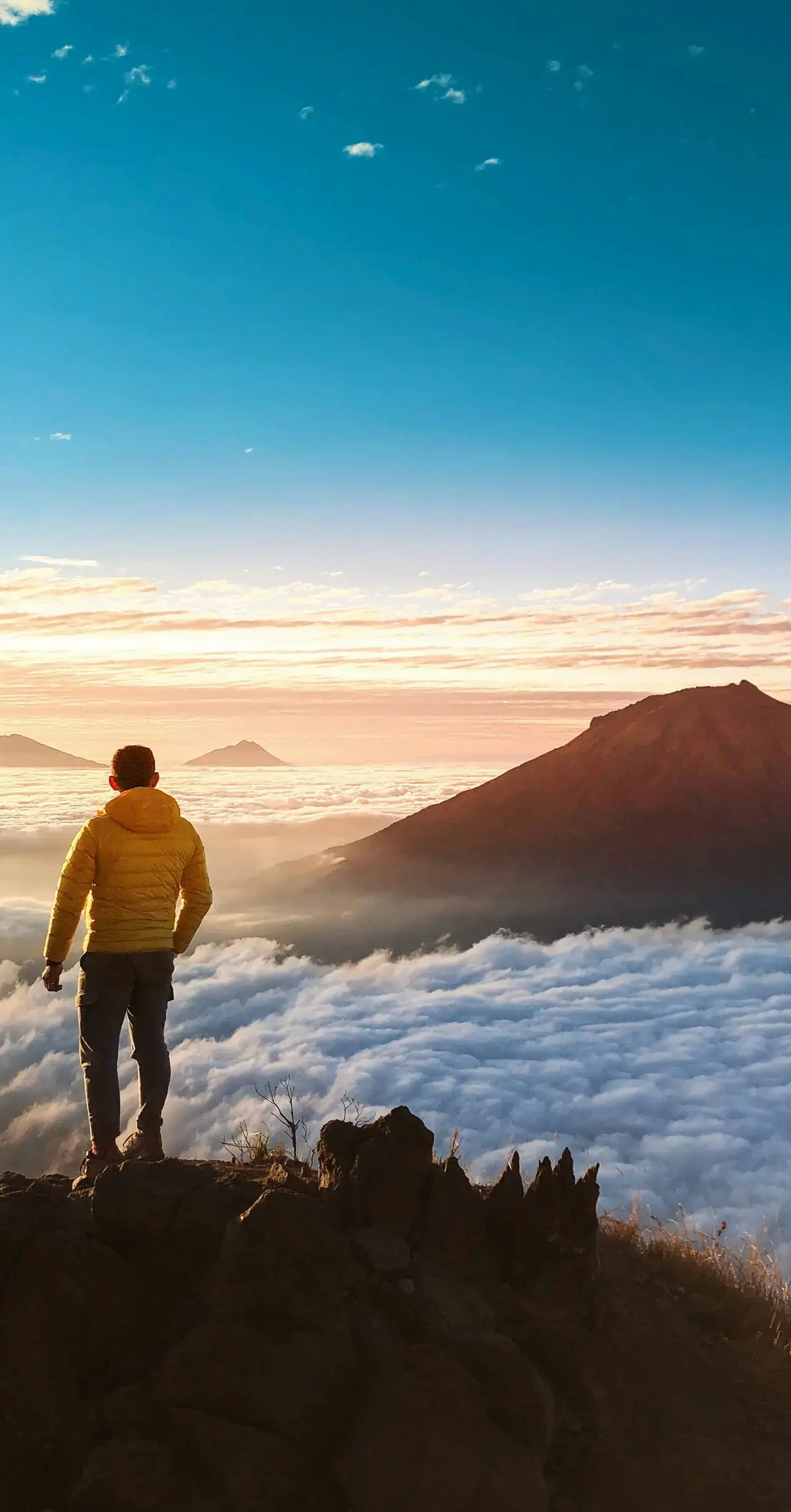 雲海に浮かぶ山々を眺める、黄色いジャケットを着た男性の後ろ姿_メインビジュアル_sp