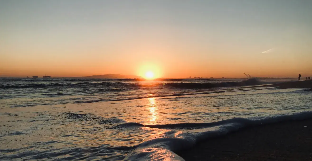 地平線に沈む夕日と、海岸に打ち寄せる白い波