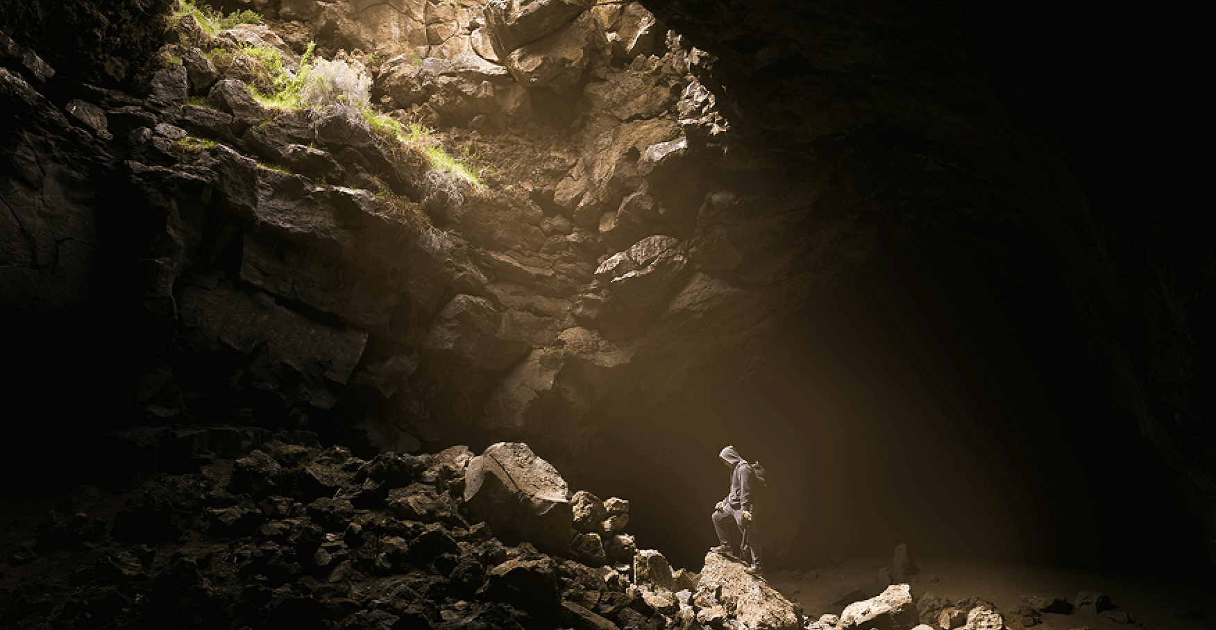 洞窟の奥で差し込む光に照らされる人物のイメージ