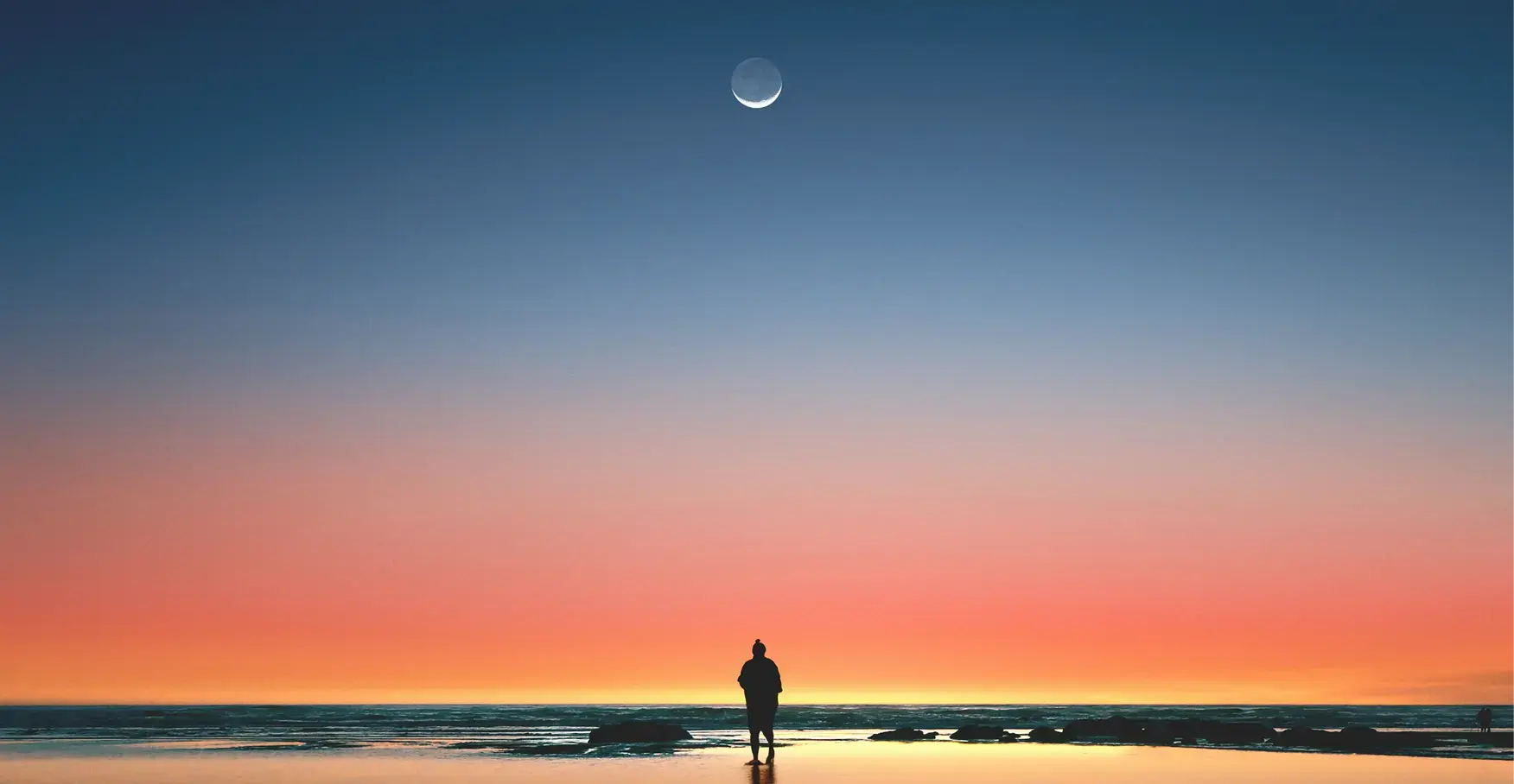 三日月が浮かぶグラデーションの美しい夕空の下、静かな海岸に佇む人物のシルエット