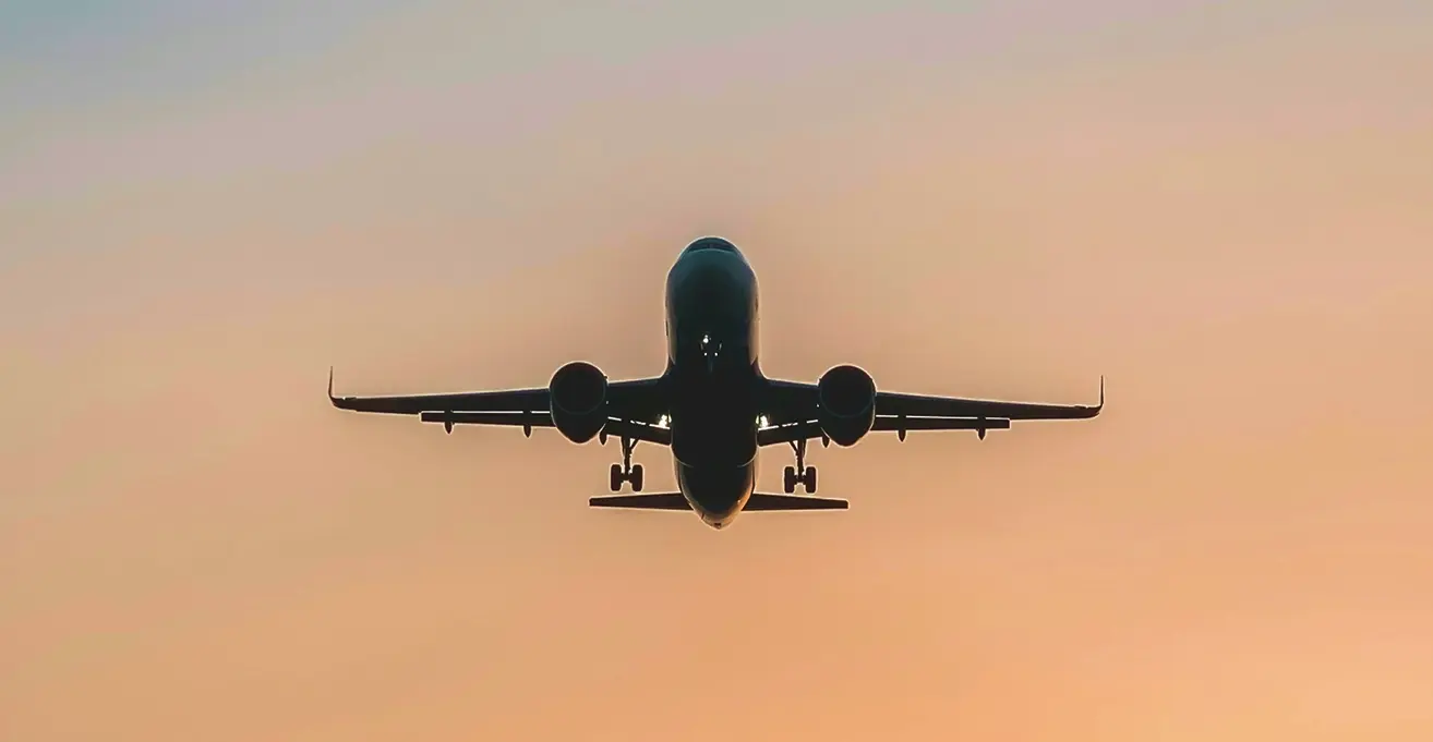 夕暮れ時のグラデーション空を背景に、ランディングギアを出して正面から迫る飛行機のシルエット