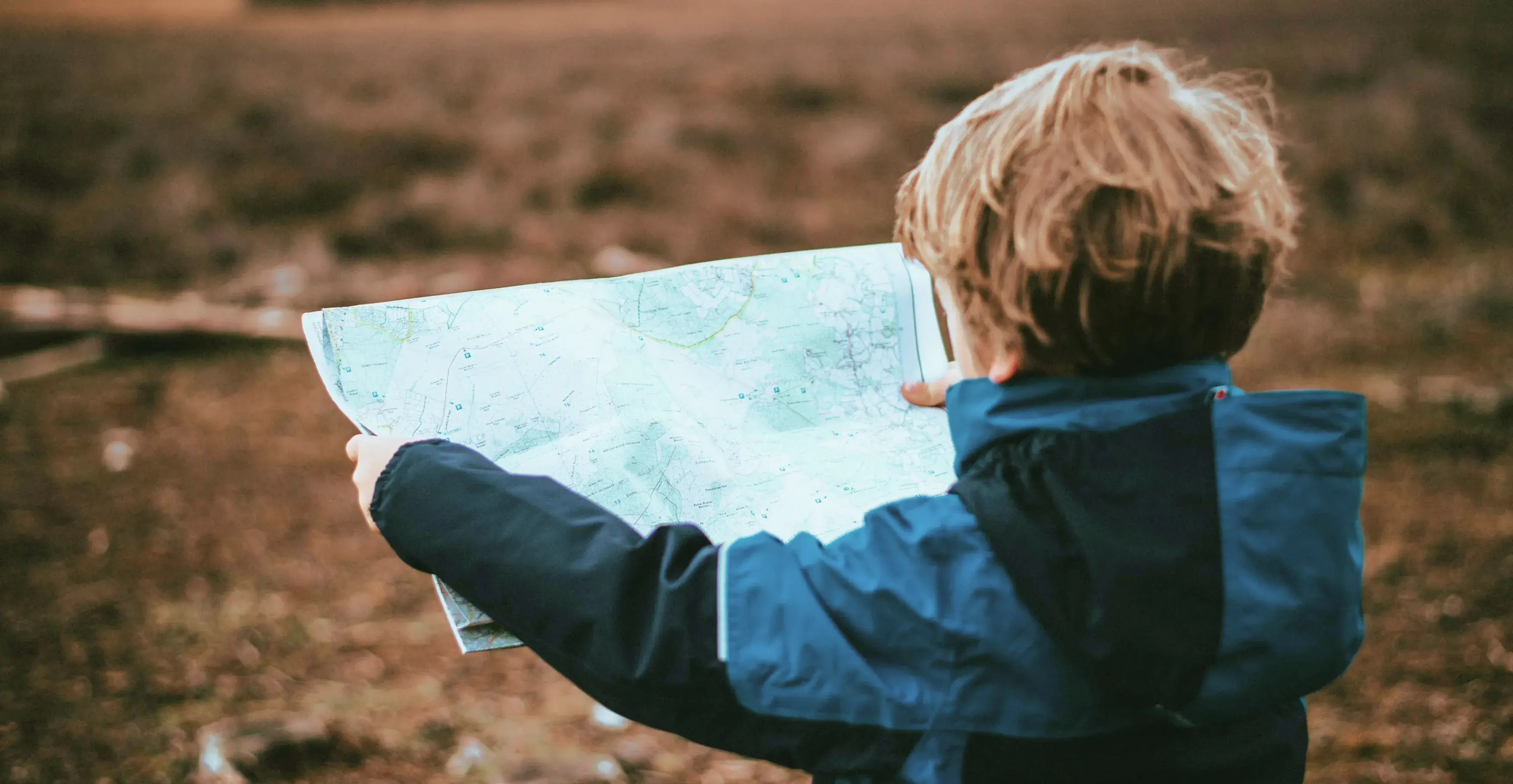 屋外で大きな地図を広げて見ている子供の後ろ姿