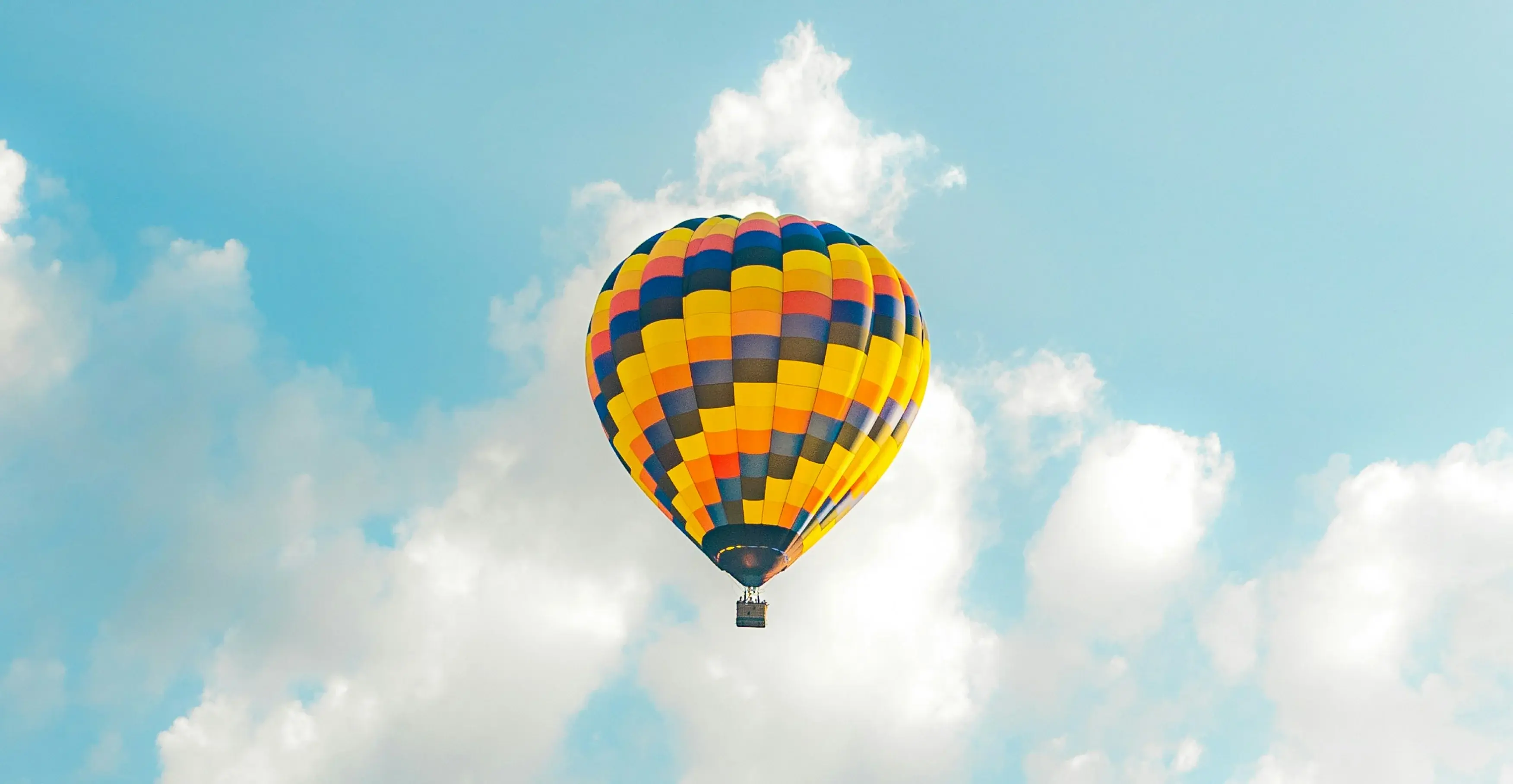 青空と白い雲の中を浮遊する、カラフルな柄の熱気球