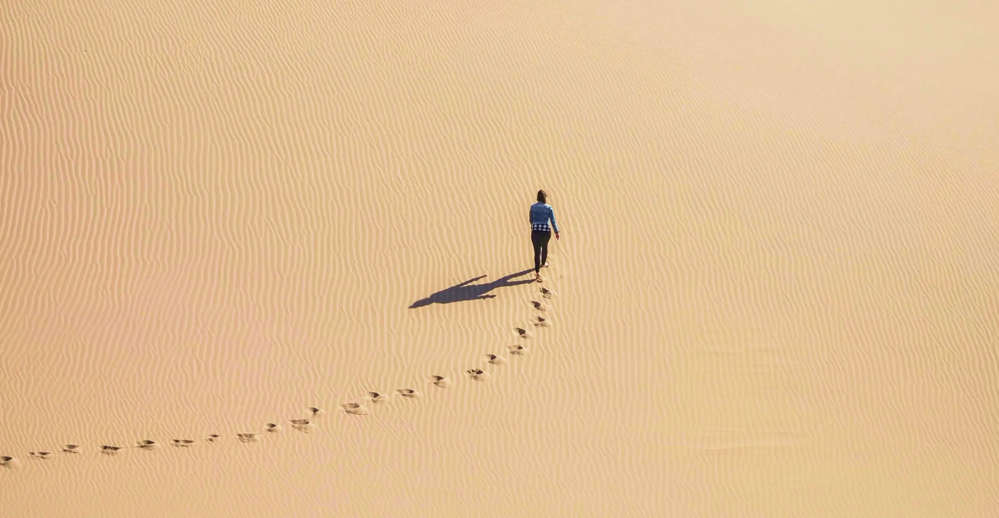 砂丘を歩く一人の人物と、砂の上に続く足跡