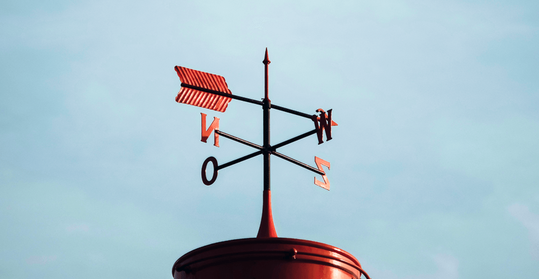 赤い風向計が青空の下で方向を示すイメージ
