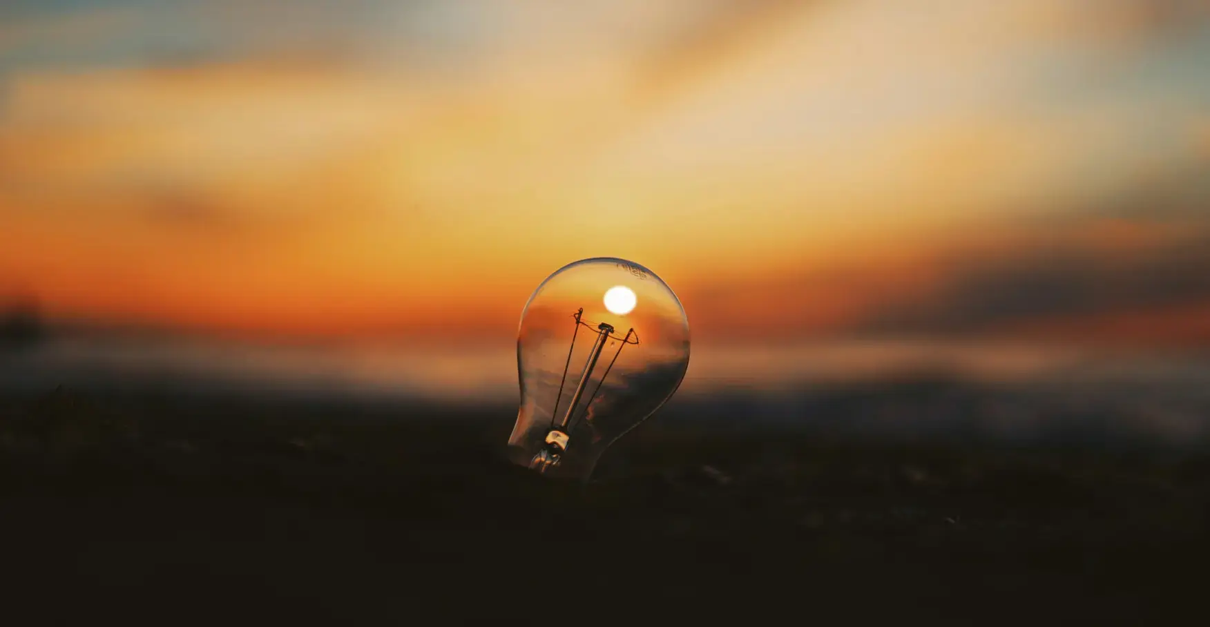 夕焼け空を背景に、内部で太陽が輝いているように見える透明な電球