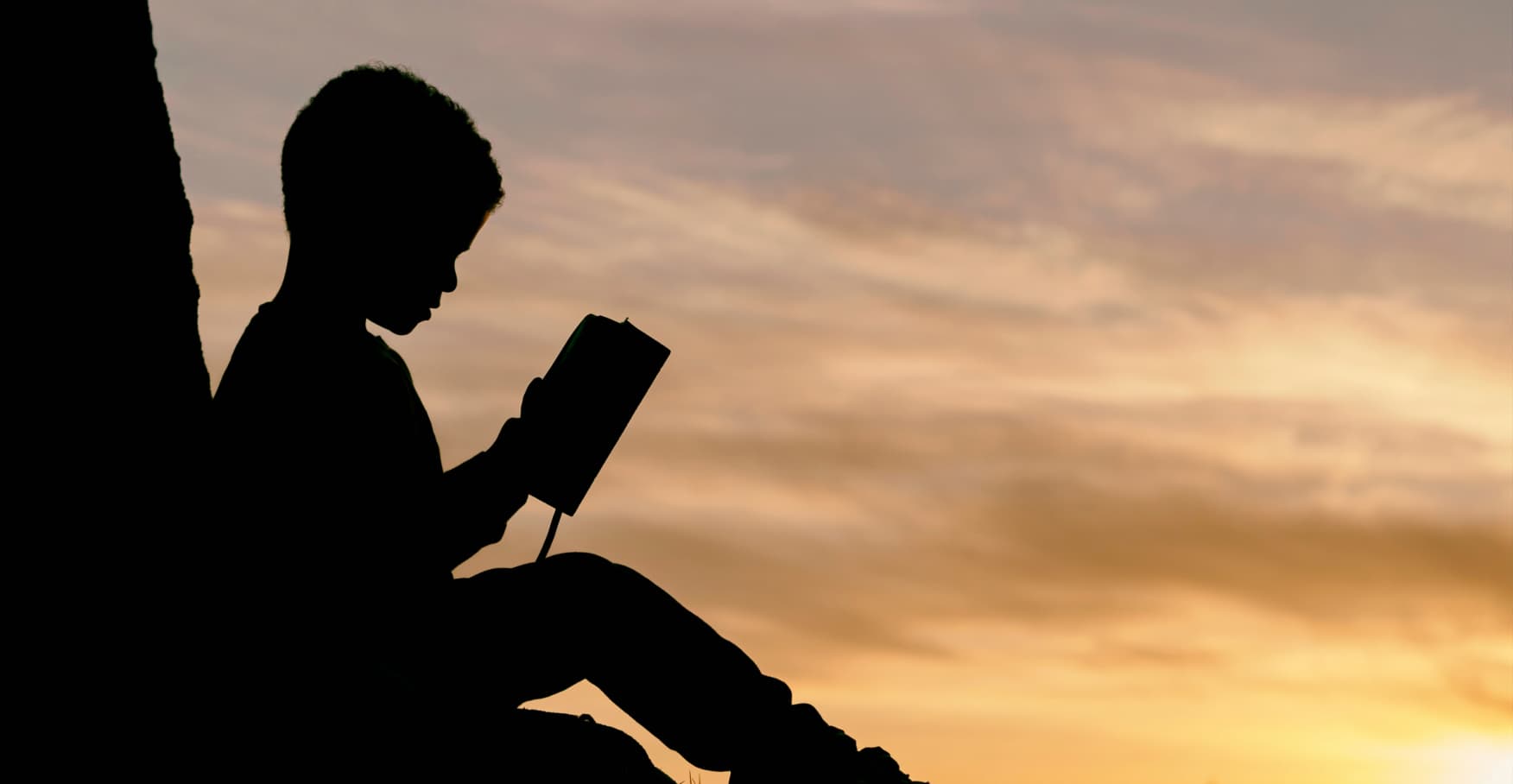 夕焼け空を背景に座って本を読む子供のシルエット