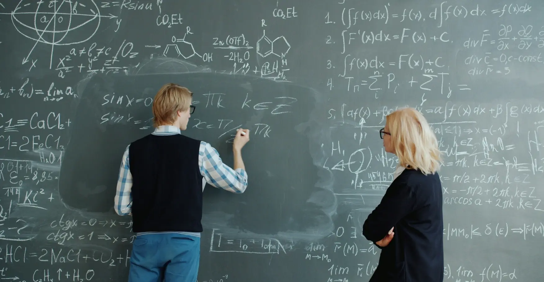 黒板の前で数式を書く人物と見守る人物のイメージ
