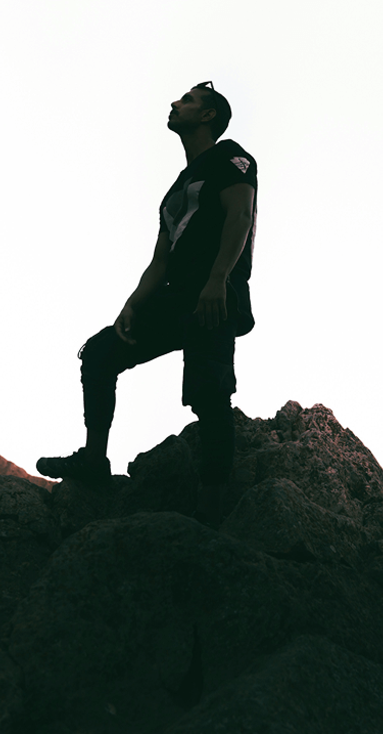 岩山の頂に立ち、空を見上げる人物のイメージ